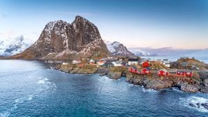 Snowy mountain landscape of Hamnøy with view of Eliassen Rorbuer cabins with bright blue sea and sky in Lofoten, Norway