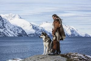 Viking man standing with husky in front of mountains in Arctic Norway
