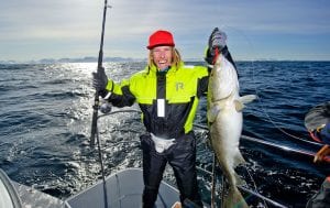Happy man with fishing rod holding up large fish caught on boat in Lyngen, Norway