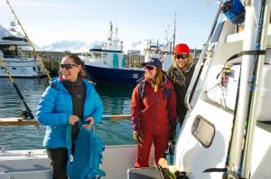 Three people with sunglasses and outdoor gear on boat smiling on a clear day