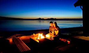 Couple sitting in front of outdoor fireplace at night, on the terrace of Lyngen Experience Lodge in Lyngen, Norway