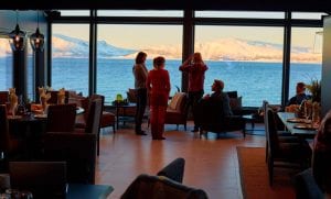 Clients chatting in living room of Lyngen Experience Lodge with a window view of the Lyngen Alps and sea in daytime