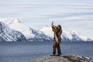 Viking man blowing into horn in front of mountains in Arctic Norway