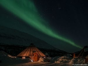 Lit up building at Camp Tamok under green northern lights in starry night sky in Lyngen, Arctic Norway