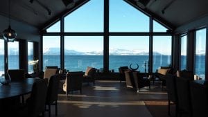 Lounge room of Lyngen Experience Lodge facing full-length window view of sea and mountains in Lyngen, Arctic Norway