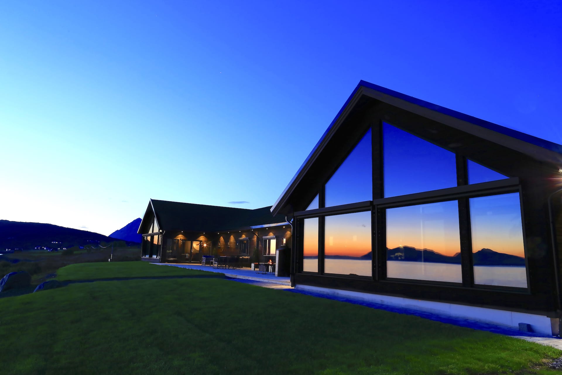 Exterior view of Lyngen Experience Lodge at sunset in summer with sea reflected off building window