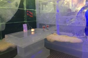 Carved ice table with two red drinks and reindeer skins on ice seats in Magic Ice Bar Tromsø