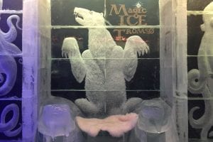 Carved words Magic Ice Tromsø on ice wall next to rearing bear ice wall sculpture with seat in Magic Ice Bar Tromsø