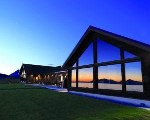 Full exterior view of Lyngen Experience Lodge in summer with full-length window reflection of sunset in summer in Lyngen, Arctic Norway
