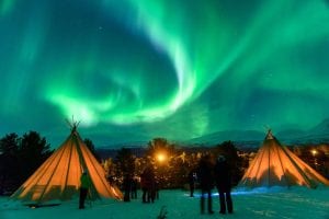 Northern Lights Aurora Borealis with people looking up at the sky and sami camp tents