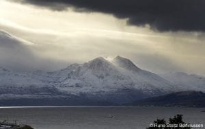Arctic Norway dark clouds and bright sky shining on snowy mountains and sea