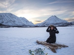 Girl sitting on reindeer skin ice fishing on frozen lake near Tromsø, Norway