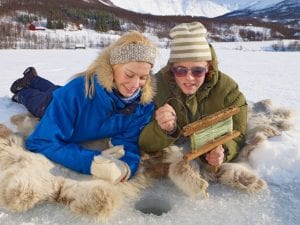 Two guests lying on reindeer skins ice fishing on frozen lake in tromsø, norway