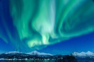 Northern Lights Aurora Borealis in the sky with snow covered fjords and trees with sea