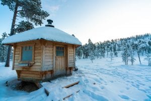 Wooden Lake Hut covered in snow with snow and snow covered trees all around with snowy footsteps