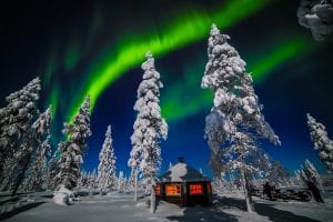 Northern Lights Aurora Borealis in the sky with a wooden snow covered cabin an snow covered trees