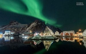 Svinøya Rorbuer Northern Lights with reflection of the buildings in the water and fjords