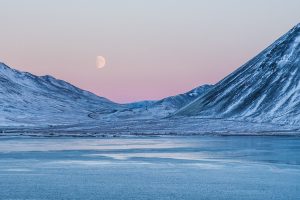 Iceland snow covered mountain fjords and lake with ice with dusk pink sky and a full moon